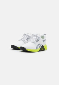 Witte sportschoenen met grijze accenten, een textiel bovenwerk en een fel geel-groene zool met een zwart loopvlakpatroon.