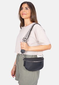 Schwarze Leder-Crossbody-Tasche mit einem Reißverschluss und strukturiertem Finish. Enthält einen gemusterten, verstellbaren Schultergurt und metallische Hardware-Details.