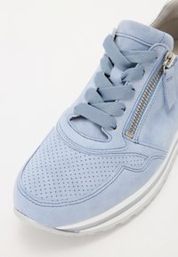 Light blue suede sneaker with perforated detailing, flat laces, side zipper, and white rubber sole. Rounded toe and smooth texture.