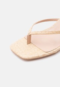 Μπεζ πλεκτή σανδάλια με τετράγωνη μύτη, λεπτές λουρίδες και λουρίδα ανάμεσα στα δάχτυλα σε ανοιχτό φόντο.