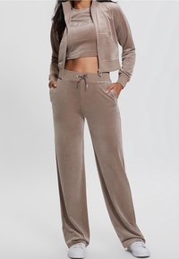 Fluwelen trainingspak in lichtbruin; cropped zip-up jack met zak, bijpassende losse broek met trekkoord en logo-detail.
