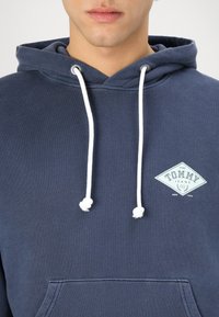 Felpa blu navy in cotone misto, con tasca frontale, cordini bianchi e un logo azzurro chiaro sul petto.