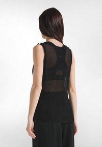 Czarny top bez rękawów z teksturowanym, plisowanym wzorem. Przezroczysta tylna część i zaokrąglony dekolt z postrzępionymi krawędziami. Gładkie wykończenie.