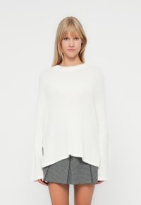 Pull blanc surdimensionné en matériau doux, avec un col bateau, des manches longues et un ourlet arrière légèrement plus long.