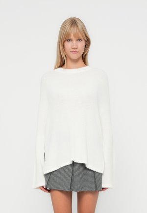 Hvit oversized genser laget av mykt materiale, med båthals, lange ermer og en litt lengre bakhem.