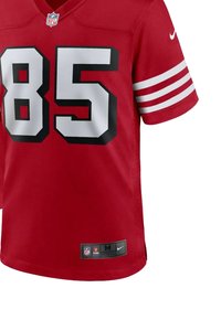 Maillot de football rouge avec des rayures blanches sur les manches, grand numéro noir 85, logo NFL sur le col et marque Nike sur l'ourlet inférieur.