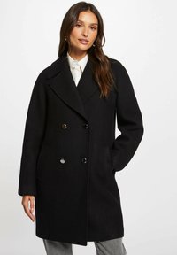 Zwarte wolmix jas met dubbele knopen, grote revers, twee vo pockets en glanzende zwarte knopen. De gestructureerde stof biedt warmte.