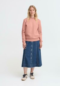 Lys rosa genser med ribbestrikkede mansjetter og midjebånd, paret med en jeanskjørt med frontknapper og lommer. Uformelle joggesko fullfører antrekket.