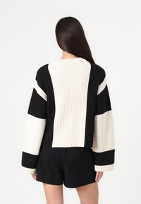 Svart og kremstripet ribbestrikket genser med lange ermer og cropped design, med bred halsutskjæring og teksturert strikket stoff.