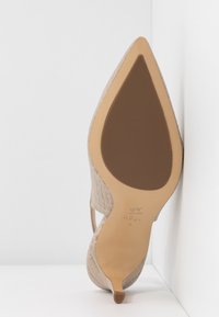 Chaussure à talons beiges avec une texture matelassée et un bout pointu, dotée d'une semelle extérieure lisse couleur tan et d'un logo discret embossé près du talon.
