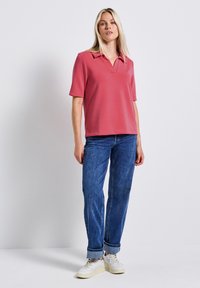 Różowa koszulka polo z krótkim rękawem i kołnierzykiem, w połączeniu z ciemnoniebieskimi dżinsami o prostym kroju i białymi sneakersami.