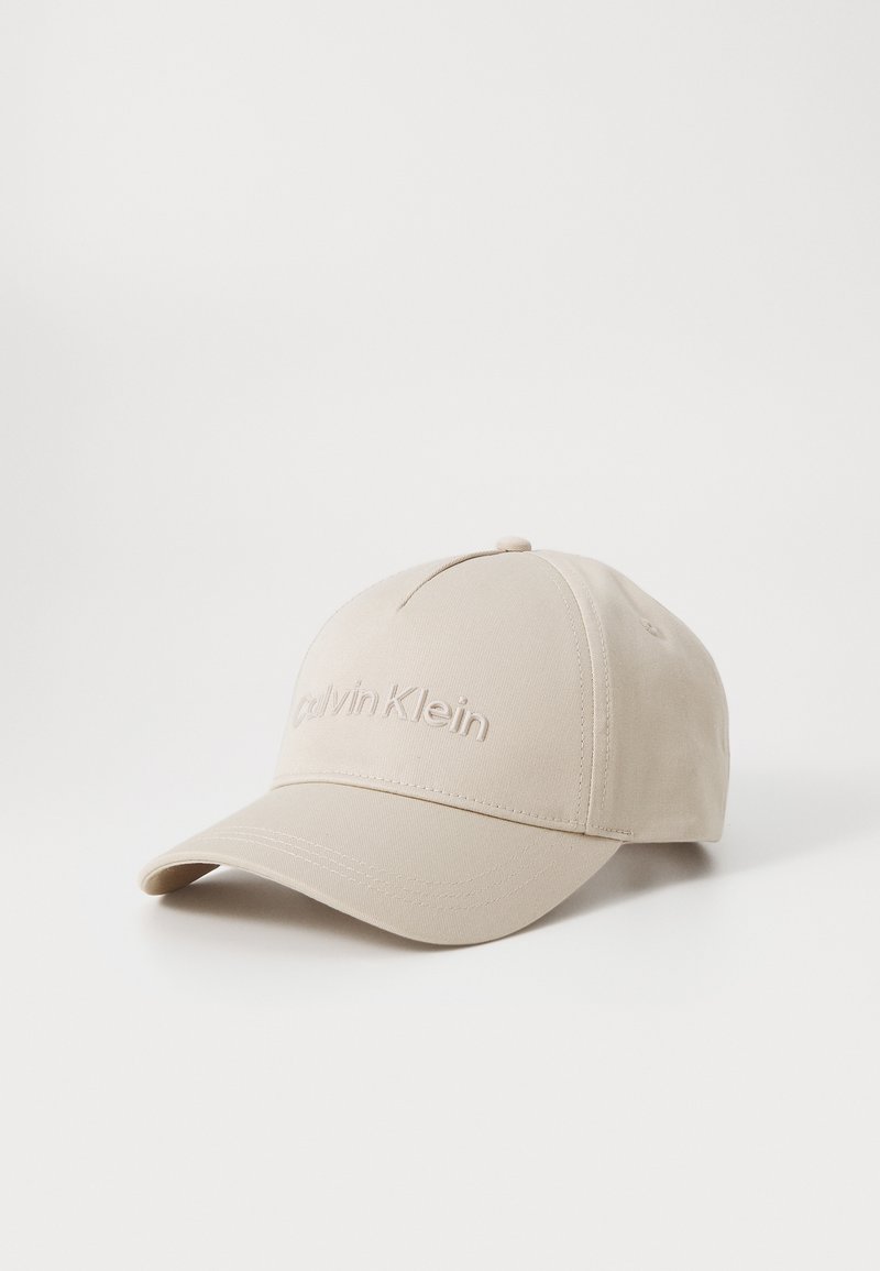 Beige caps laget av glatt stoff, med en brodert "Calvin Klein" logo foran, buet skygge og justerbar stropp bak.