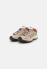 Baskets de sport beige et orange avec une tige en mesh respirant, une semelle extérieure texturée noire et un système de laçage rapide pour un ajustement facile.