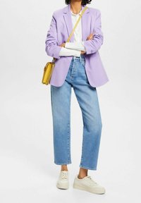 Ljuslila blazer över en vit skjorta, i kombination med ljusblå raka jeans och krämfärgade sneakers. En liten gul crossbody-väska fulländar looken.