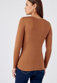Lange mouwen bruine shirt van zacht materiaal, met een ronde halslijn en een slanke pasvorm, gecombineerd met donkerblauwe jeans.