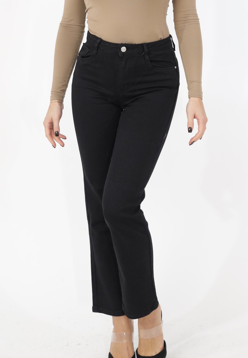 Jean taille haute noir avec une coupe droite, poches avant et fermeture par bouton argenté ; assorti à un haut nude à manches longues.