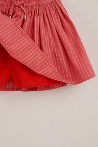 Rot-weiß gestreifter Rock mit elastischem Bund und Kordelzug, darunter sind rote, angenähte Shorts aus Stoff zu sehen.