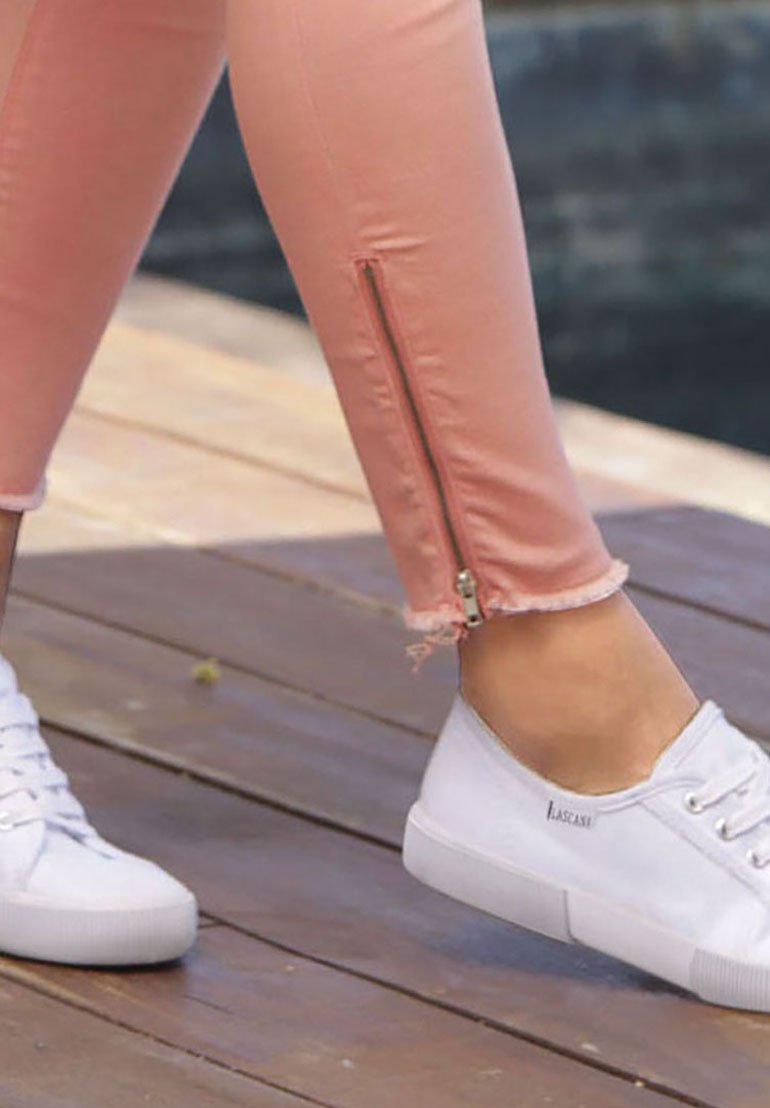 Pink leggings with a side zip feature at the ankle, frayed hem, paired with white sneakers featuring a textured sole and laced design.