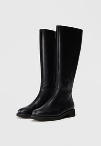Botas de cuero negro hasta la rodilla con punta redonda, cierre de cremallera lateral, costuras mínimas y una suela plana resistente.