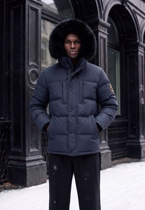 Homme portant une doudoune bleu marine avec une capuche bordée de fourrure, debout les mains dans les poches dans une rue enneigée devant un bâtiment noir orné.