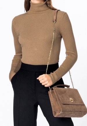 Kobieta ubrana w brązowy prążkowany golf i czarne spodnie, trzymająca brązową zamszową torebkę z złotym łańcuszkowym paskiem i zapięciem.