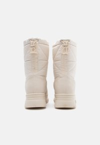 Botine bej cu umplutură, cu vârf rotund, material texturat și un tab de prindere pe spate; material impermeabil; talpă plată, antiderapantă.