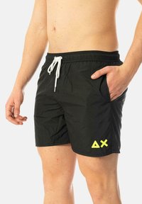 Costumi da bagno neri realizzati in materiale leggero, con vita elastica e cordoncino, tasche laterali e un logo geometrico giallo brillante.