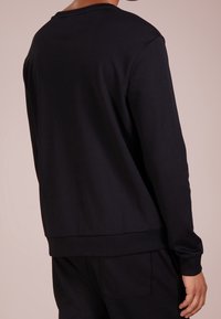 Schwarzes Sweatshirt mit Rundhalsausschnitt, gerippten Bündchen und Saum, glatter Textur und minimalen Nahtdetails. Nur Rückansicht.