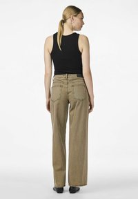 Jeans beiges de tiro alto y pierna ancha con dos bolsillos traseros, detalles de costura y una etiqueta negra en la cinturilla. Combinados con una camiseta de tirantes negra.