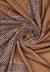 Tessuto marrone con un motivo a spirale che presenta forme circolari in bianco, accentuato da sottili linee bianche. Morbida texture, materiale leggero.