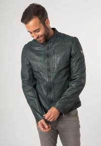 Giacca in pelle teal da uomo con zip frontale e tasche, texture rigata sulle spalle e colletto alto. Design moderno e aderente.