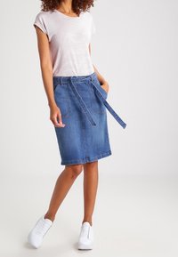 Falda de mezclilla con cintura anudada, que cuenta con dos bolsillos frontales. Combinada con una camiseta a rayas y zapatillas blancas. Look general casual.