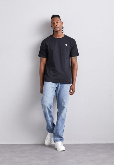 Svart bomull t-skjorte med korte ermer og rund hals, med en liten hvit logo. Kombinert med lyseblå denimjeans og hvite joggesko.