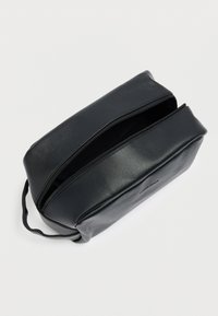 Μαύρο δερμάτινο τσαντάκι με ομαλή υφή, ορθογώνιο σχήμα και κλείνει με φερμουάρ. Διαθέτει μικρή λαβή στη μία πλευρά.