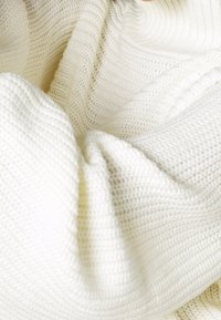 Mjuk vit stickad filt med texturerade mönster; har en ribbad kant och en löst vävd struktur som förstärker dess mysiga utseende.