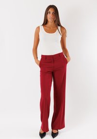 Pantaloni rossi a gamba larga con una trama liscia e una vestibilità su misura. Abbinati a un top senza maniche bianco e scarpe nere con punta affusolata.