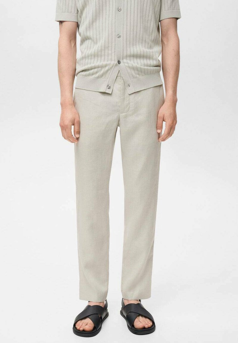 Pantaloni in lino color beige chiaro con un design a gamba dritta, abbinati a un top in maglia a maniche corte dello stesso colore e sandali neri.
