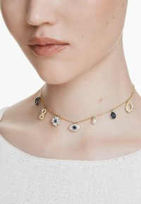 Zlatý náhrdelník s řetízkem, který obsahuje více přívěsků: černý půlměsíc, symbol nekonečna, květinu, oko, perlu, slzu a podkovu, zdobený drahokamy.