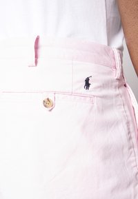 Světlé růžové šortky vyrobené z bavlny, s knoflíkovým zapínáním a malým námořnickým modrým vyšitým logem koně na zadní kapse.