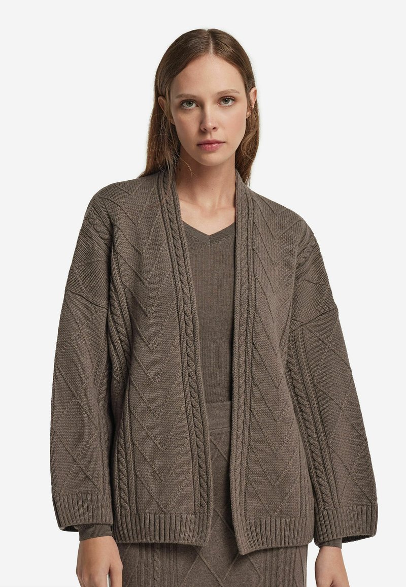 Breiter Cardigan mit Schalkragen aus strukturiertem, mittelbraunem Strick mit Zickzackmustern und gerippten Bündchen. Kombiniert mit einem passenden Oberteil.