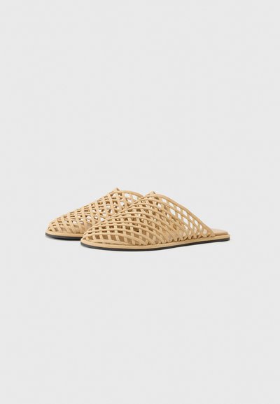 Des claquettes tissées à bout ouvert en matériau beige clair, avec un design en treillis entrecroisé et une semelle plate.
