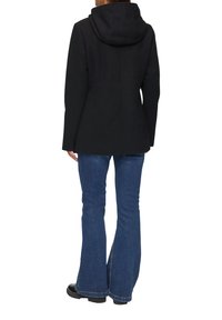 Zwarte hoodiejas met een getailleerde pasvorm, voorzien van een soepele textuur en gestructureerde naden, gecombineerd met blauwe flared jeans en zwarte schoenen.