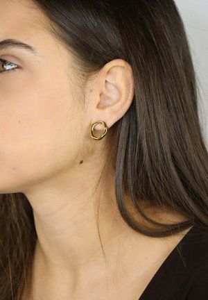 Orecchini a cerchio color oro con un design organico e intrecciato. Superficie liscia e lucida con una forma ad anello continuo.