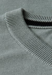 Ljusgrå stickad tröja med ribbat rundhalsat krage och en subtil textur. Kragen har en kontrasterande svart kantdetalj.