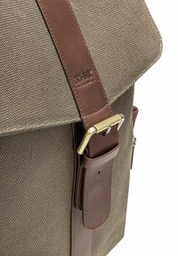 Plecak z płótna z brązowym skórzanym paskiem i mosiężnymi detalami klamry, teksturowana tkanina oraz z logo marki wytłoczonym na skórze.