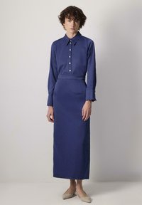 Abito lungo blu navy con colletto a punta, chiusura a bottoni e dettagli delle maniche a onda. Realizzato in tessuto morbido e testurizzato, con una silhouette aderente.