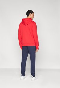 Κόκκινο φούτερ με κουκούλα, συνδυασμένο με σκούρο μπλε αθλητικό παντελόνι και λευκά αθλητικά παπούτσια. Ύφασμα απαλό με ριμπ μανσέτες και μέση.