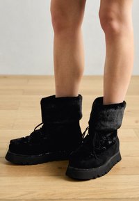 Fekete bokacsizmák műszőrme gallérral, tartós talppal és fűzős kialakítással. Texturált anyag fényes részletekkel és vastag talppal.