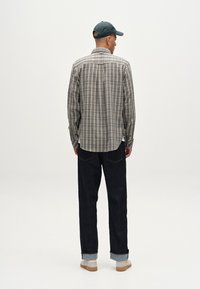 Cămașă carourile în nuanțe de bej și gri, cu mâneci lungi și tiv curbat. Asortată cu blugi negri și adidași deschiși la culoare. O pălărie verde simplă, văzută din spate.