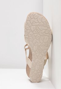 Sandale compensée beige avec semelle texturée et lanières tissées, présentée verticalement sur un fond blanc avec coins.